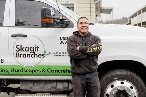 Worker standing with arms crossed beside a white Skagit Branches service truck outdoors.