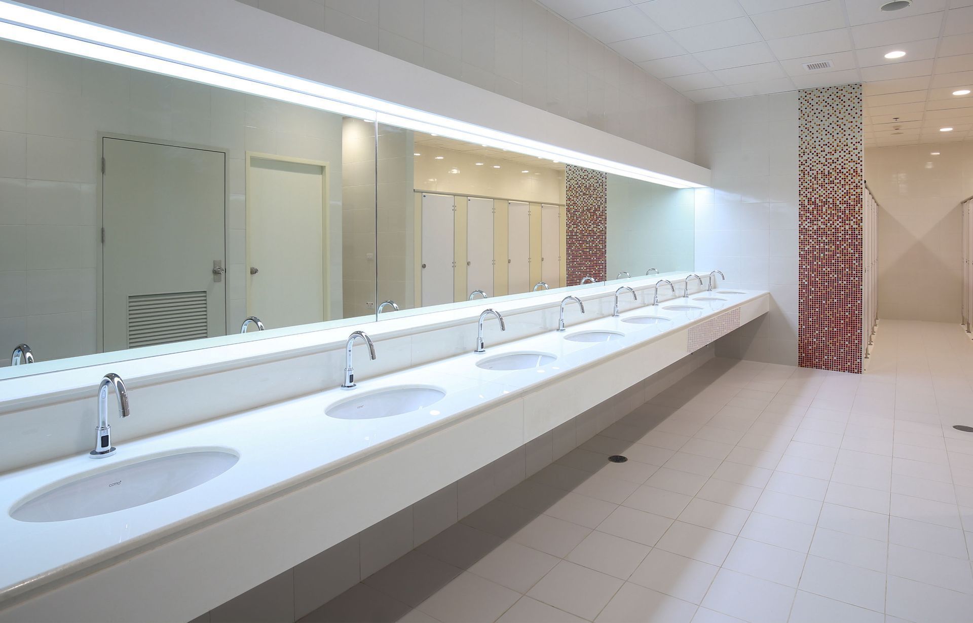 Public restroom with long white counter, sinks, and large mirror.