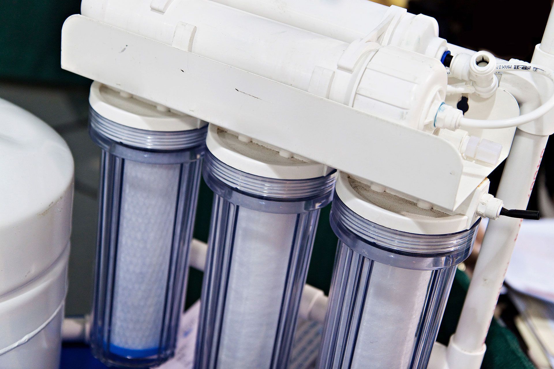 Water filtration system with three clear, cylindrical filter housings and white pipes.