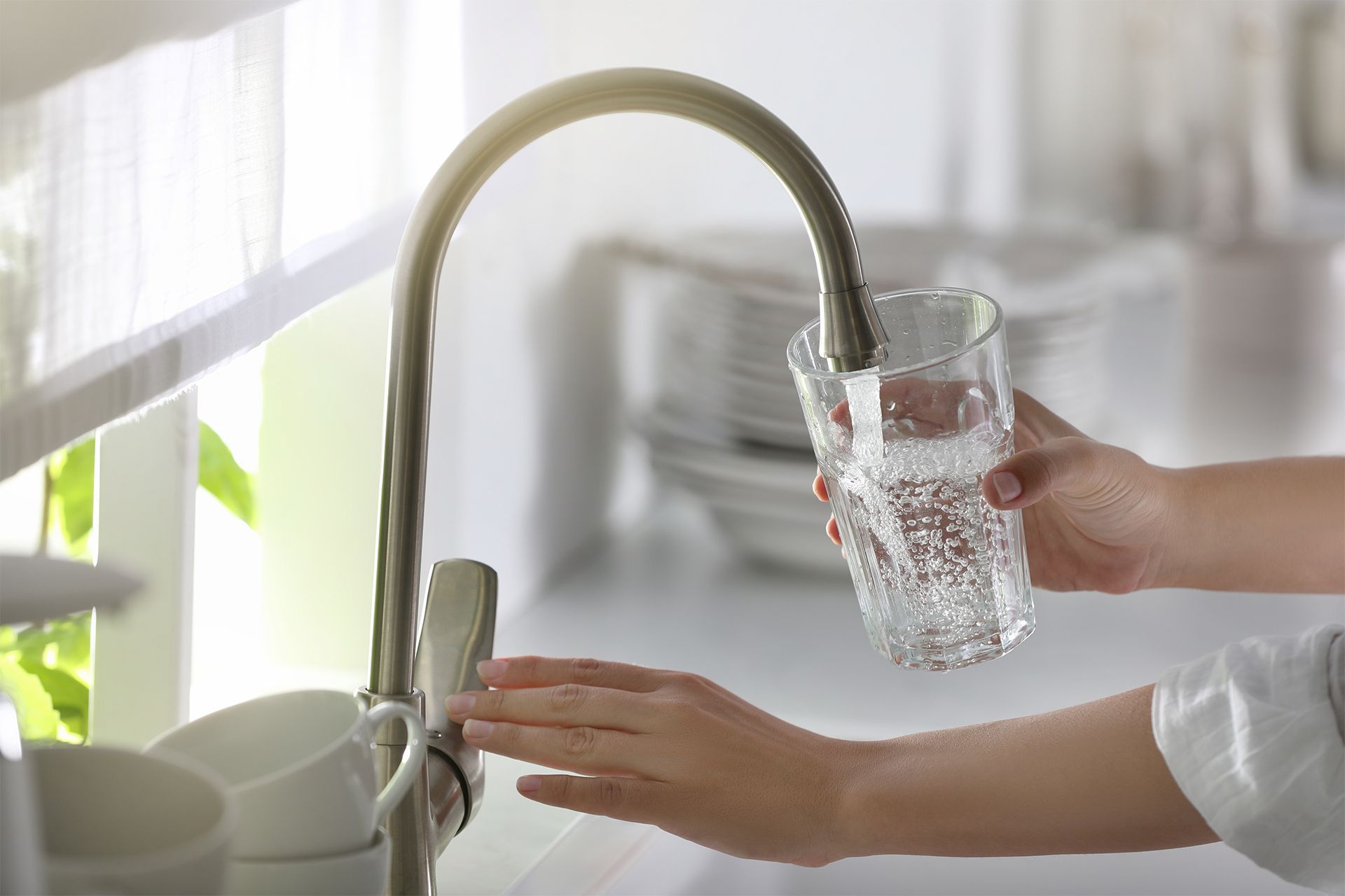 Person filling a glass with water from a kitchen faucet.