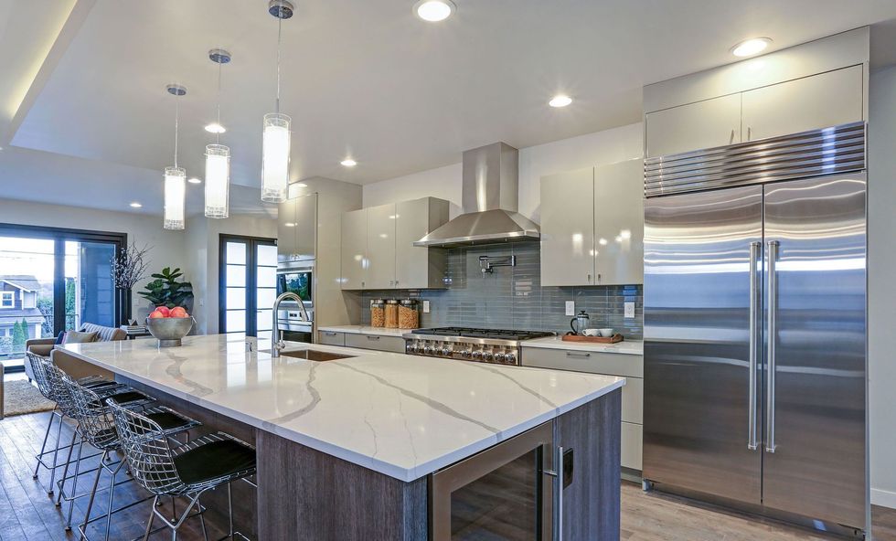 Modern kitchen with island, stainless steel appliances, and gray cabinets; open to a seating area.