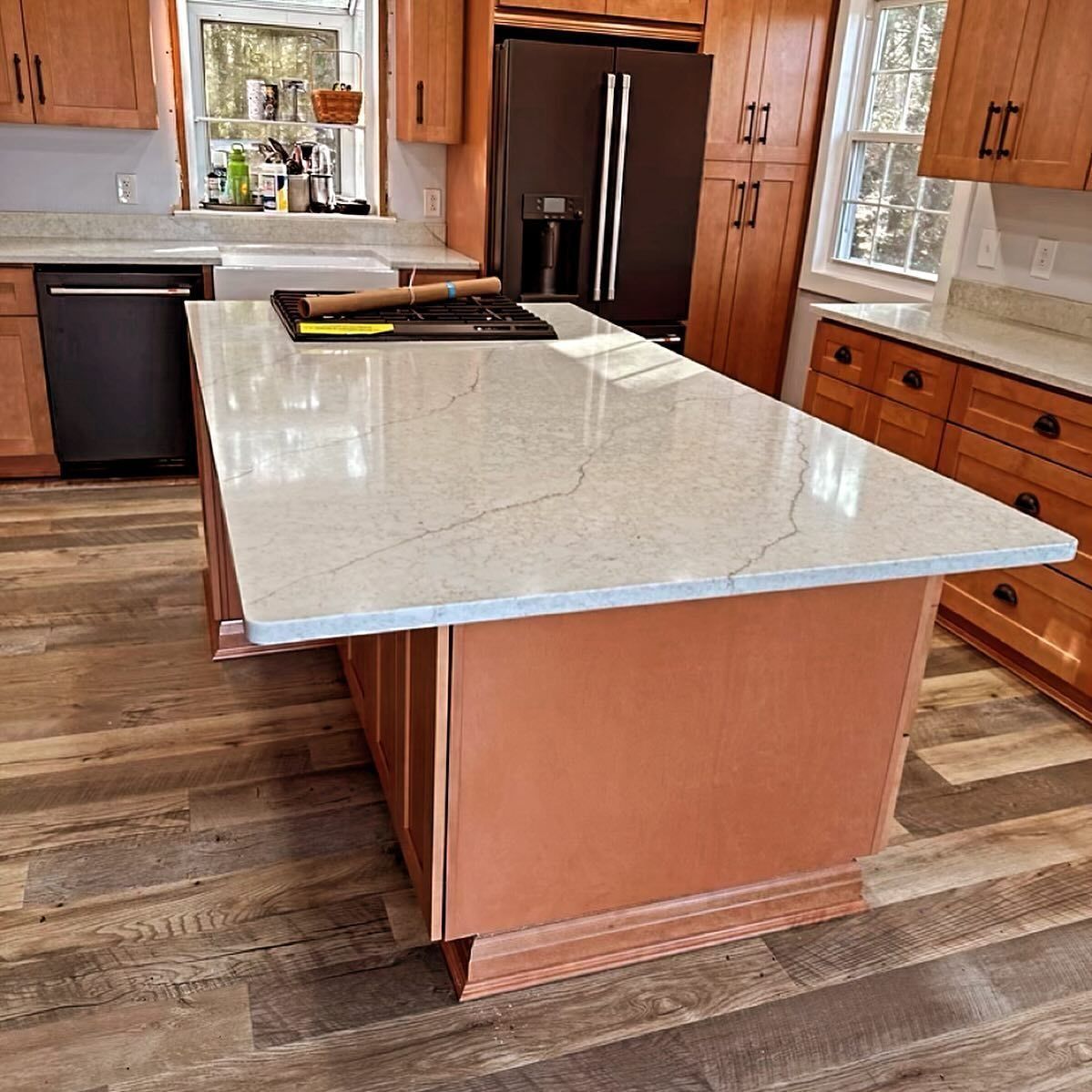 A kitchen with a large island featuring a light countertop, surrounded by wooden cabinets and flooring.