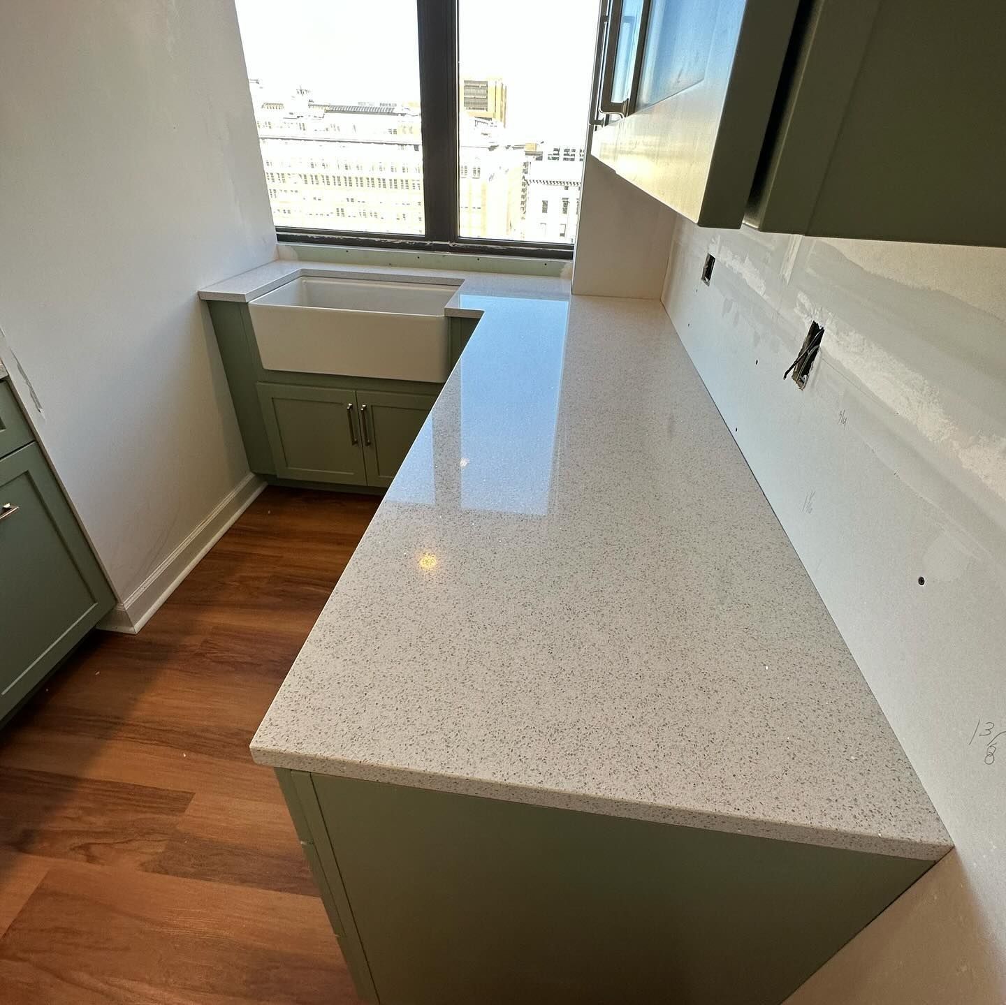 Kitchen with light quartz countertop, sage green cabinets, and a farmhouse sink by a window.