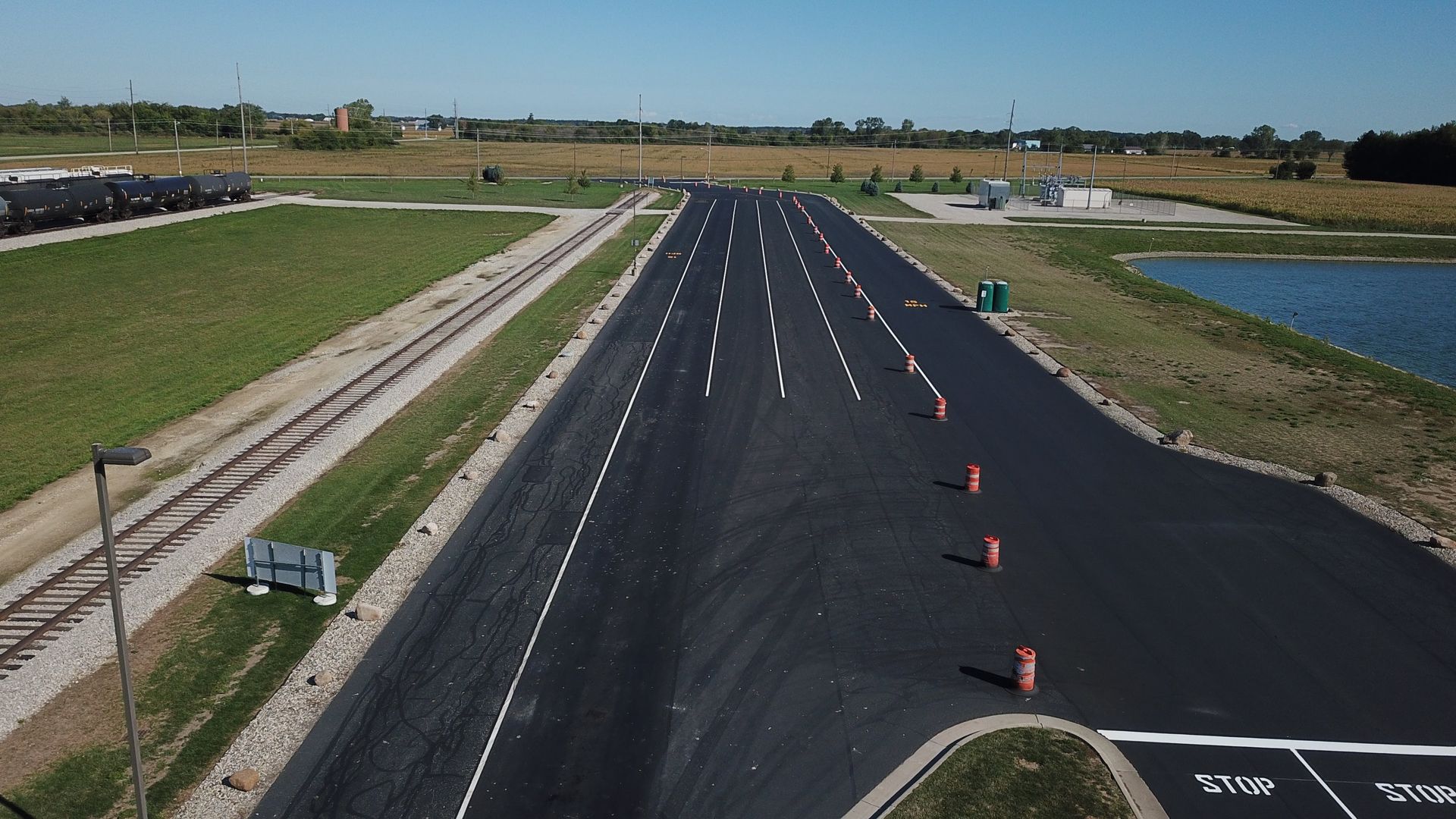 Empty paved test track with orange cones, grassy fields, and a water channel under clear sky