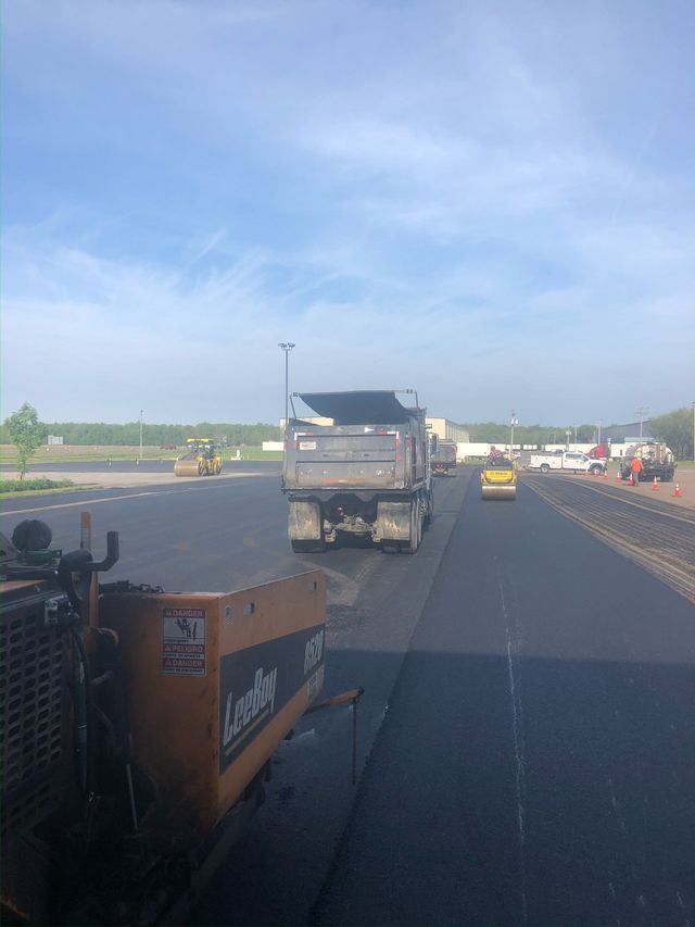 Roadwork scene with a dump truck, orange barricade, and cars on a highway under a blue sky