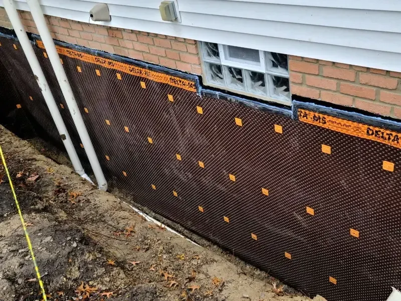 Foundation wall covered with black dimpled waterproofing membrane beneath a brick house exterior