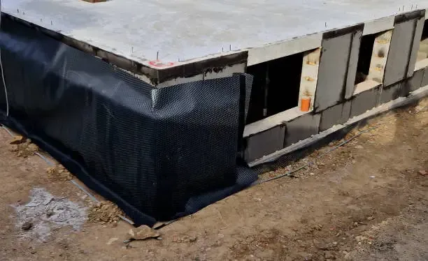 Partially finished building with black wrap and white exterior panels on bare ground