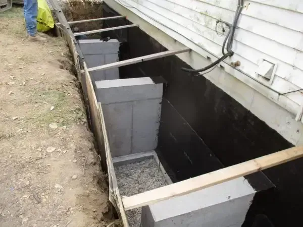 Basement wall excavation with concrete block foundation repair under a house exterior