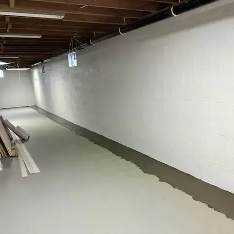 Empty basement corridor with white cinderblock walls and a newly poured concrete floor