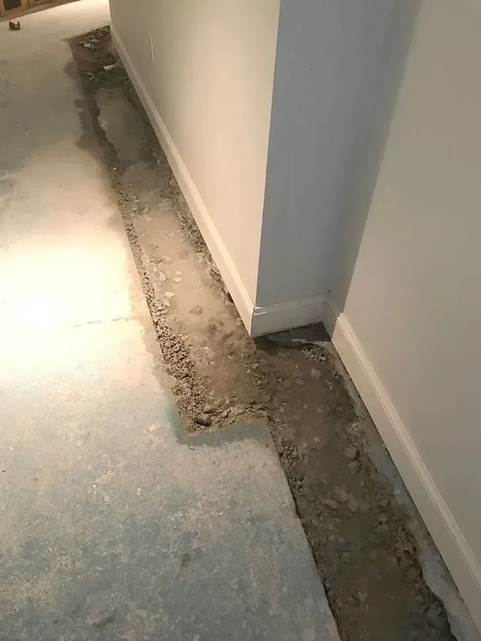 Damaged floor with a long broken trench beside a wall and doorway threshold
