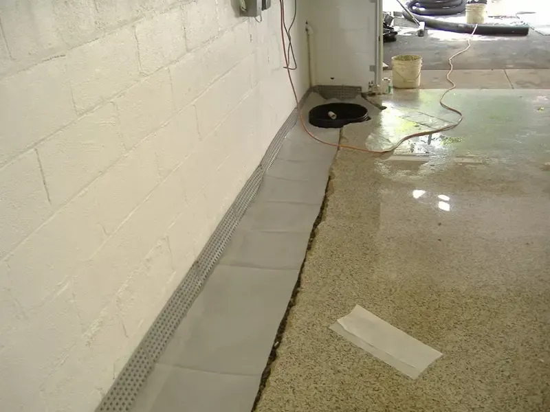 Indoor concrete floor beside white wall with a floor drain and a dark spill or hole near the wall