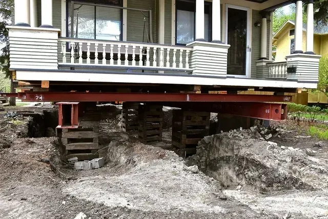 House lifted on temporary supports during foundation repair, with rubble and exposed ground beneath the porch