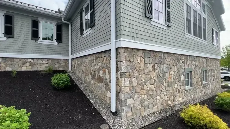 House exterior with stone foundation, gray siding, and dark mulch landscaping