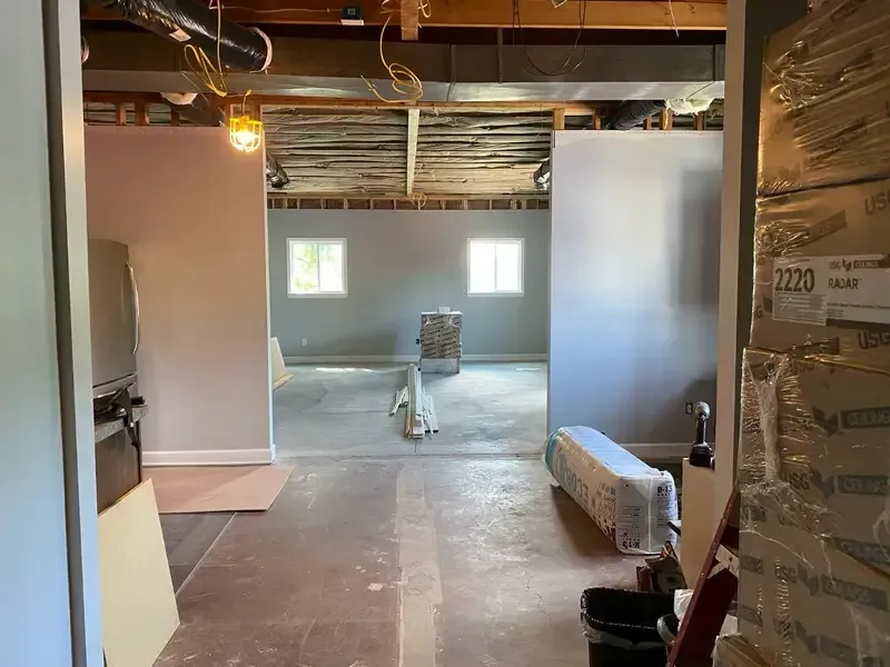 Unfinished basement with exposed ceiling, construction materials, and frosted glass doors leading to a lit room
