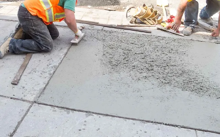 Construction workers smoothing wet concrete on a sidewalk beside large slab joints