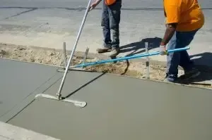 Workers smoothing fresh concrete with a long-handled trowel on a street repair site