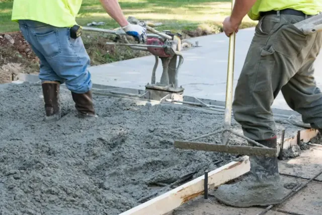 Workers pouring wet concrete at a construction site with a power trowel and screed
