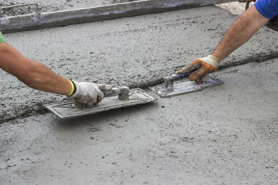 Two workers smoothing wet concrete with trowels on a construction site
