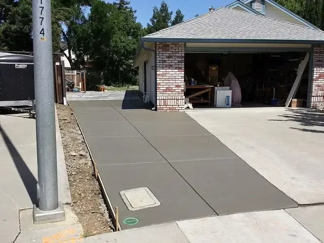 Concrete driveway ramp beside a garage, with a utility pole and sidewalk access path.