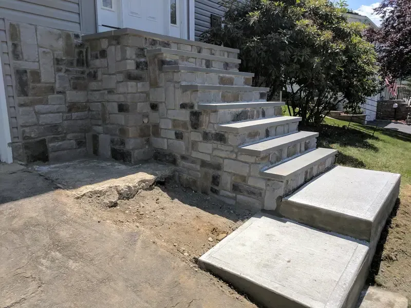 Stone front steps and retaining wall beside a house, with a newly poured concrete walkway.