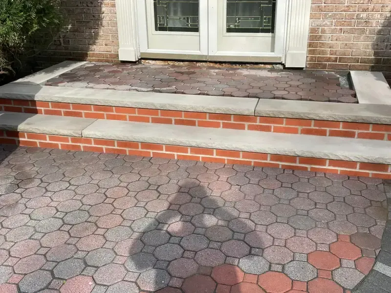Front steps to a brick house, with a patterned stone walkway and dark shadow in the foreground