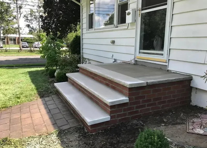 Brick front steps with white treads leading to a house entrance beside a lawn and walkway