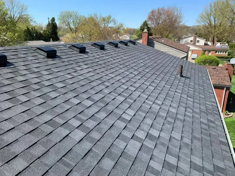 Gray shingled roof with vents and chimney, viewed from above on a sunny day