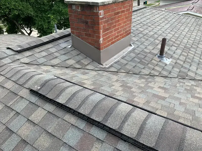 Roof with gray shingles, a brick chimney, and a vent pipe on a sloped house roof.