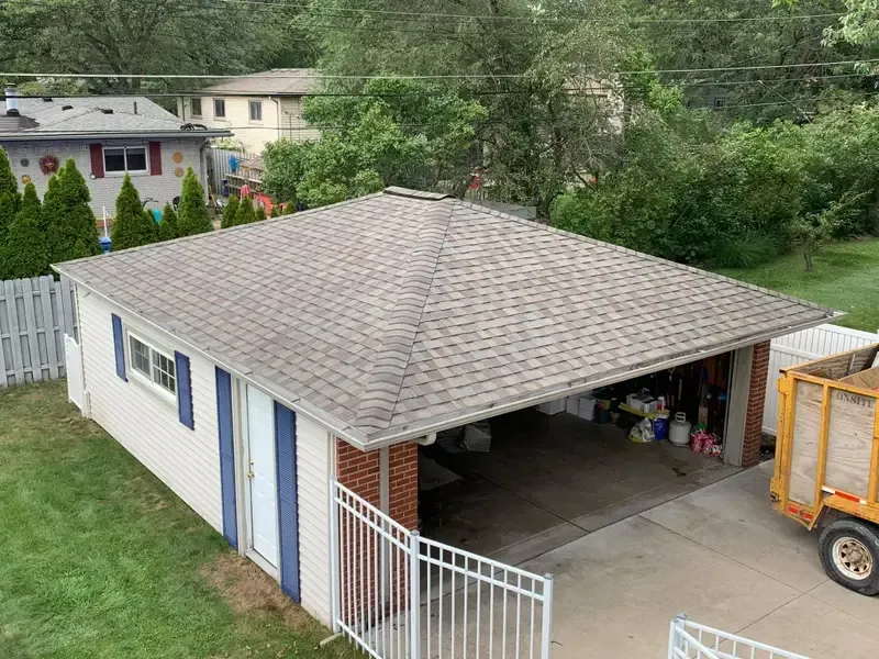 White detached garage with open bay, gray shingle roof, fenced yard, and orange truck at right