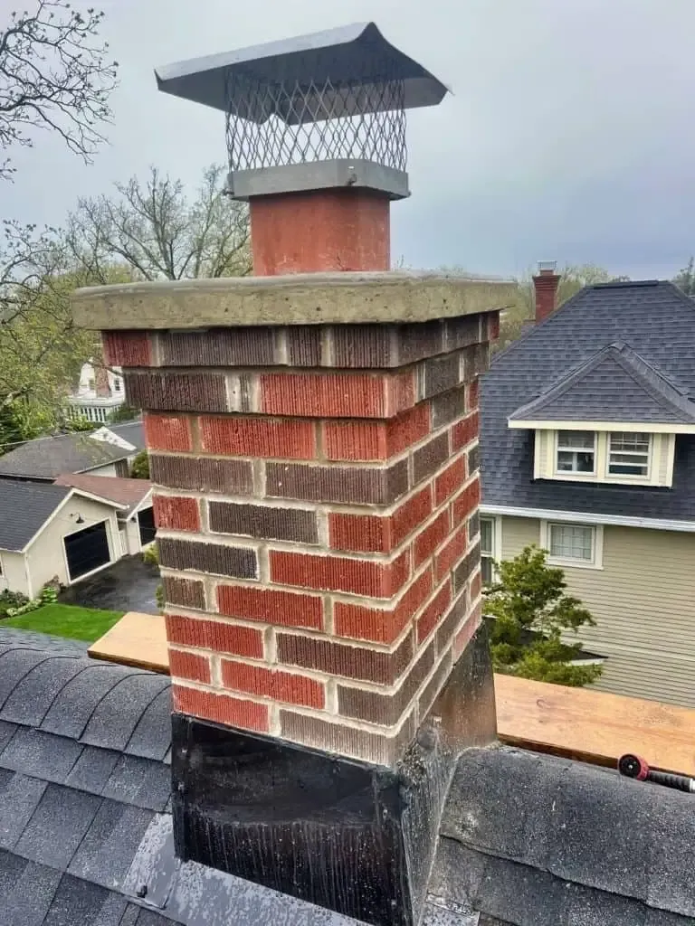Brick chimney with a metal cap on a shingled house roof, viewed from above.