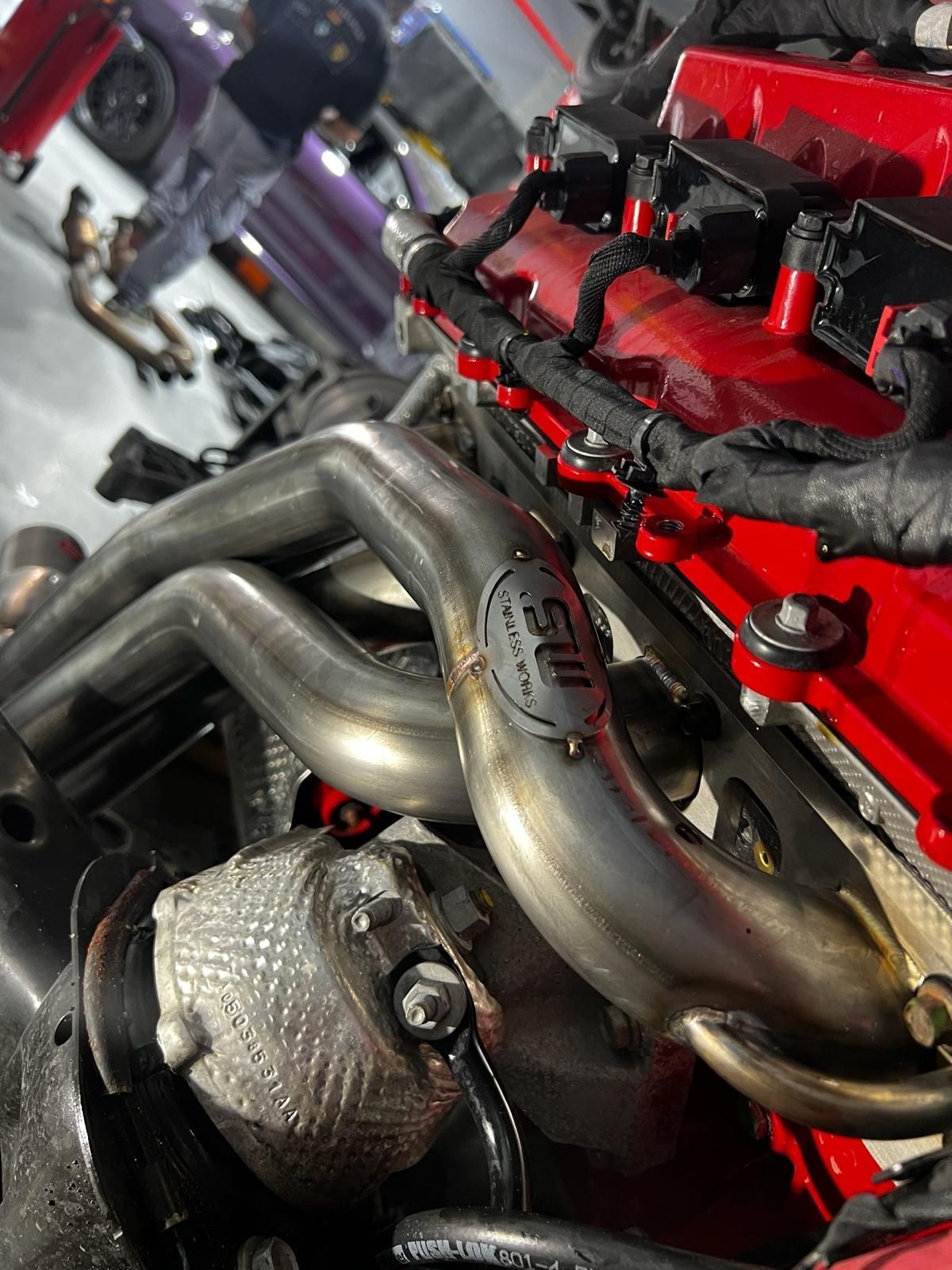 Mechanic working under a car, inspecting the exhaust system. Gloves and work overalls are worn.