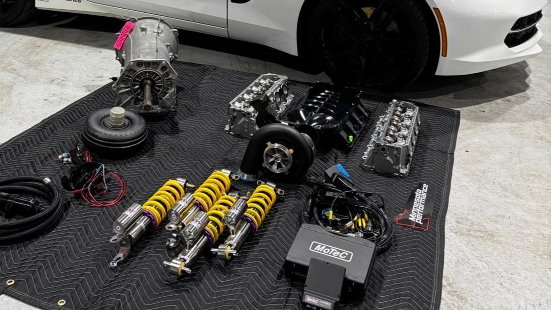 Red car with open hood, tools on a table; mechanic working.