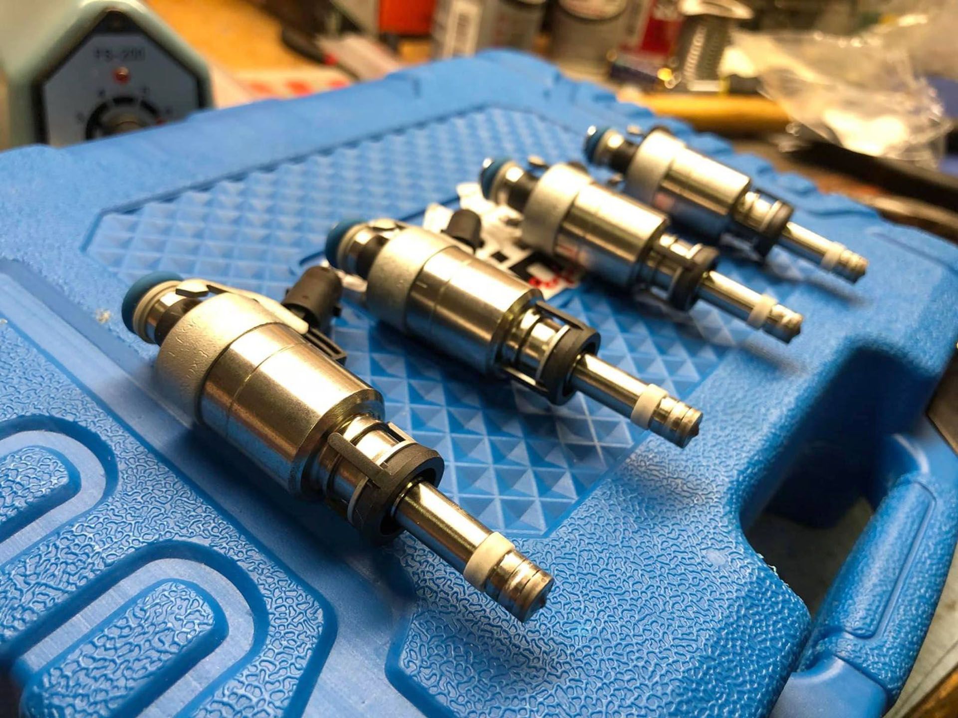 Four automotive fuel injectors arranged in a row on a blue plastic tool case