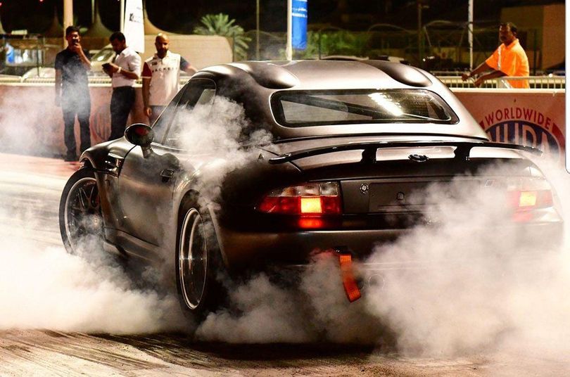 A dark sports car performs a burnout, filling the track with smoke