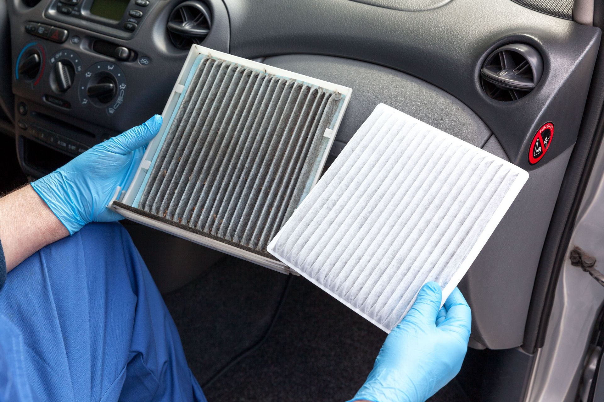 Hands in blue gloves holding a dirty and a new car cabin air filter. Interior car setting.