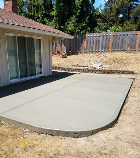 Concrete patio beside a house with sliding glass doors and a wooden fence in a backyard