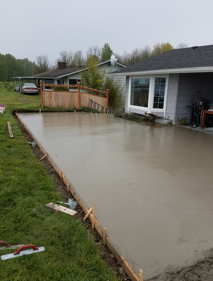 Freshly poured concrete patio beside a house with a wooden deck and grassy yard