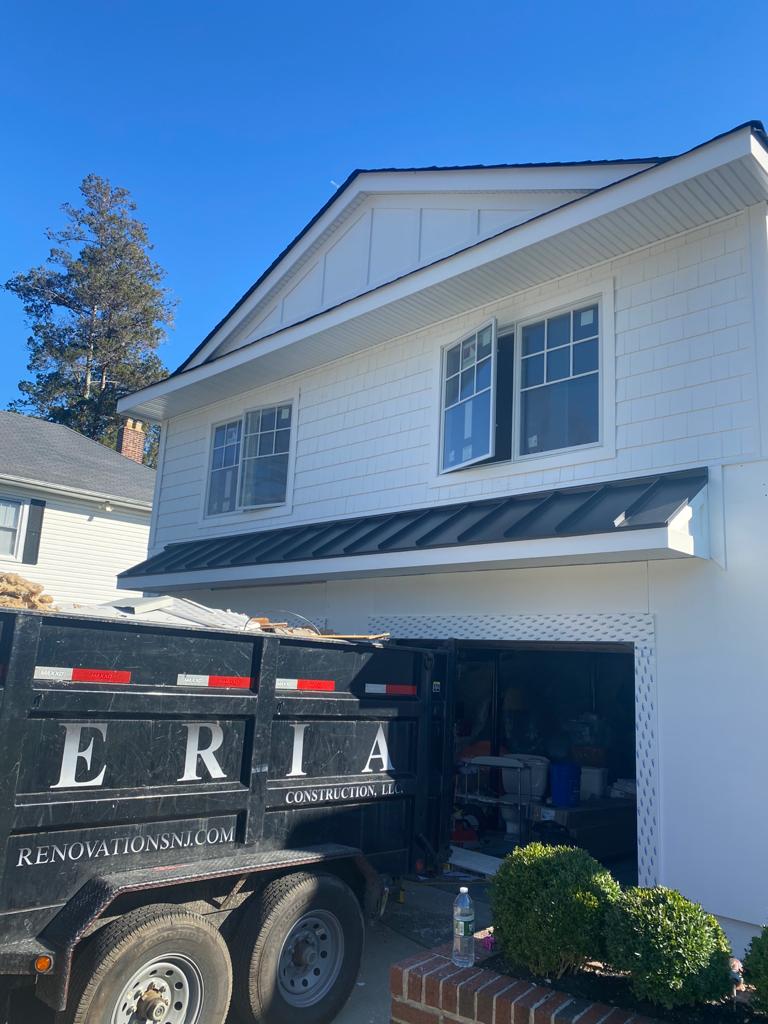 A dumpster is parked in front of a white house.