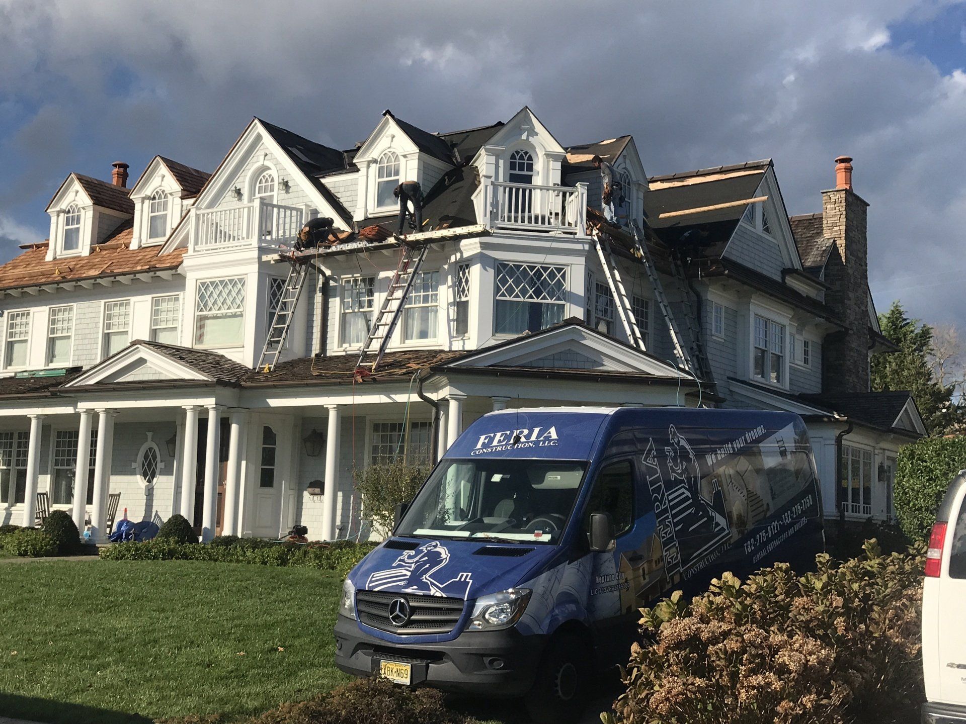 A blue van is parked in front of a large white house.