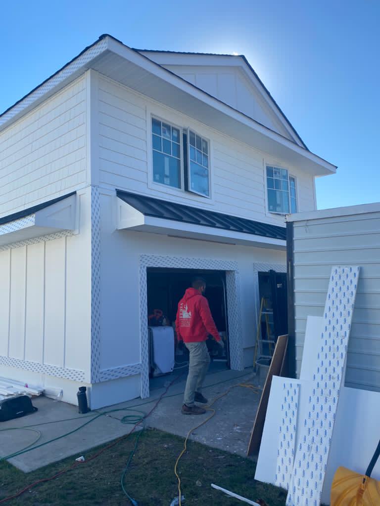 A man in a red jacket is standing in front of a white house.