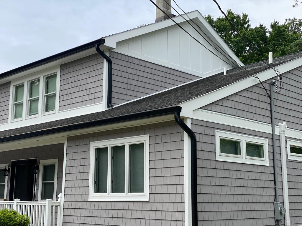 A gray house with white trim and a black gutter on the side of it.