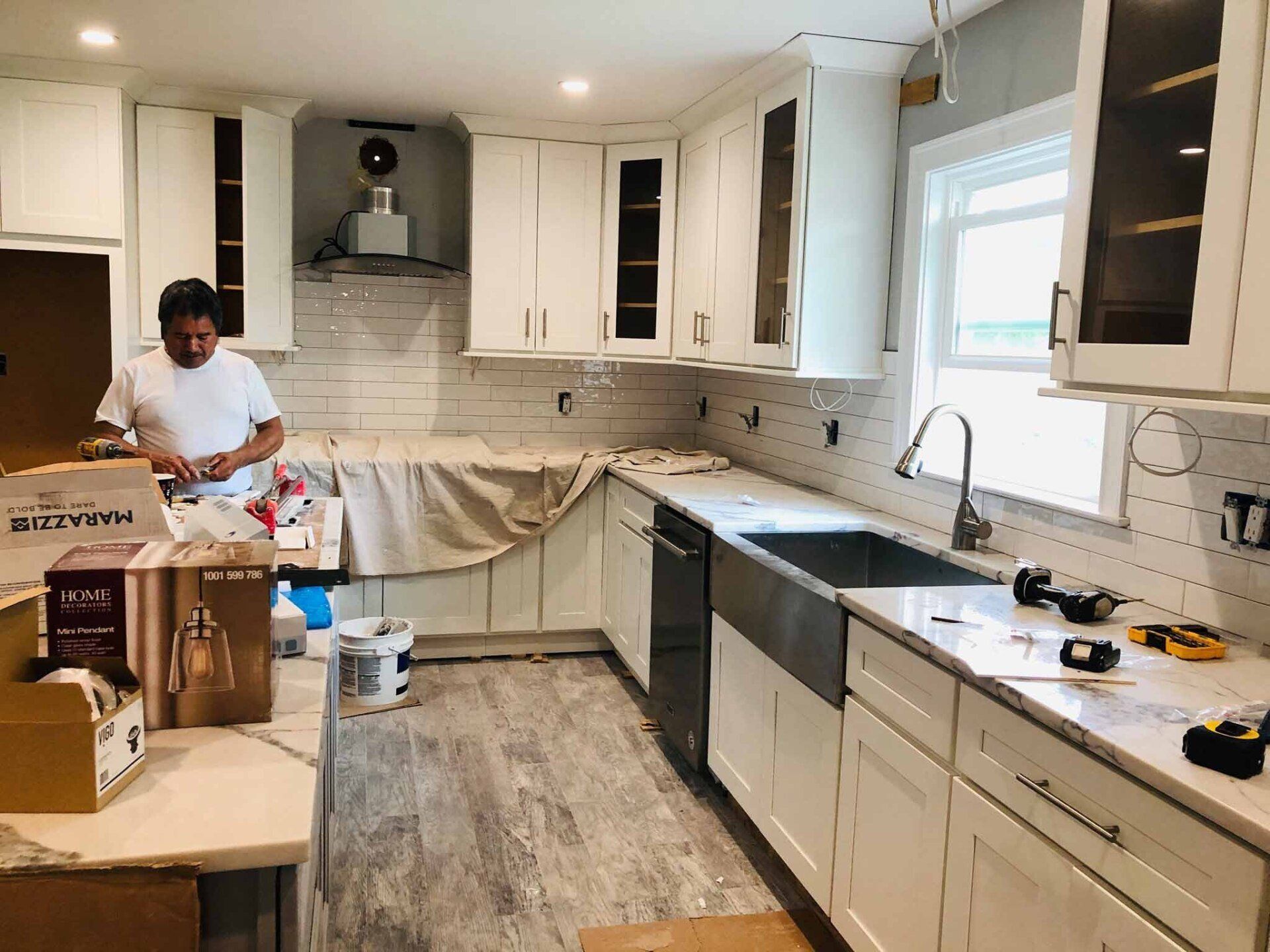A man is working in a kitchen with white cabinets and a sink.