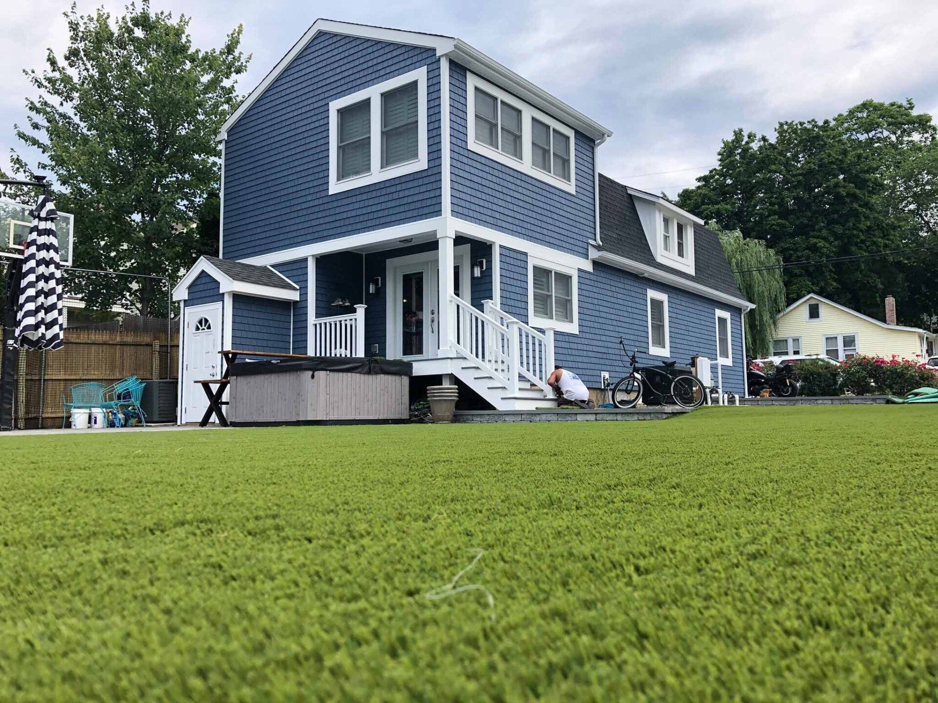 A blue house with white trim is sitting on top of a lush green lawn.