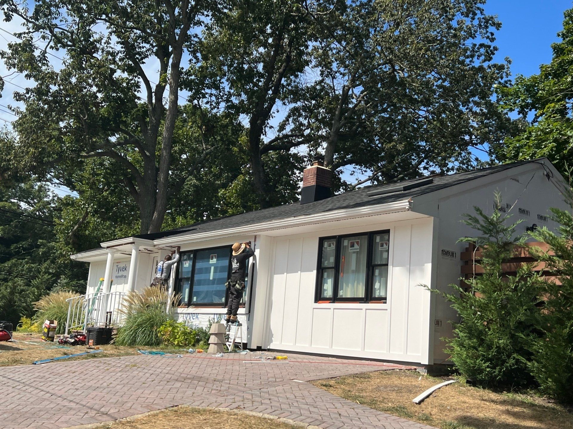 A white house with a black roof is surrounded by trees.