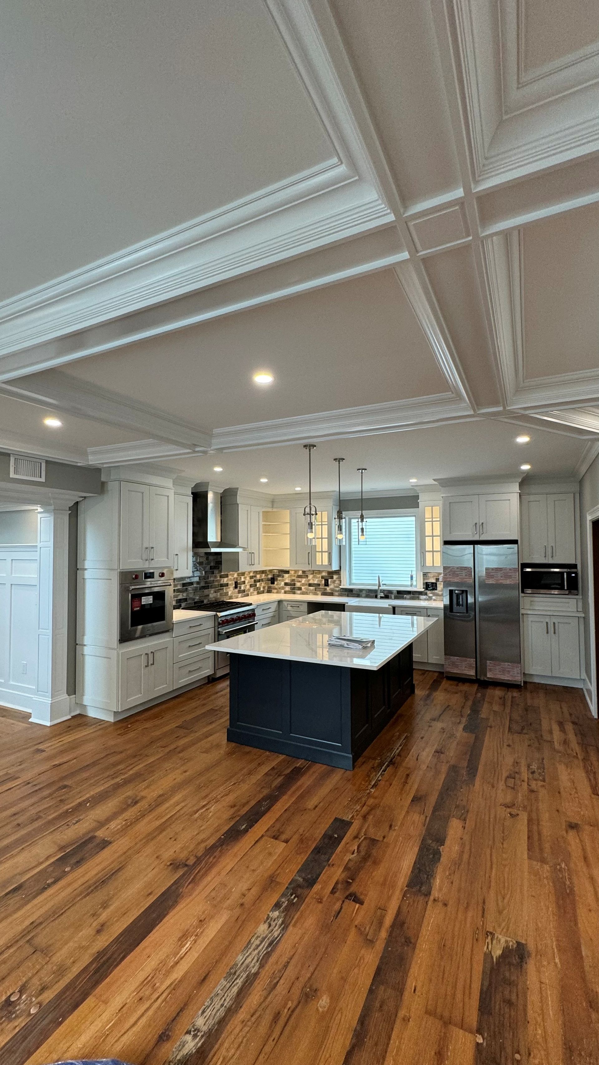 A kitchen with hardwood floors , white cabinets and stainless steel appliances.