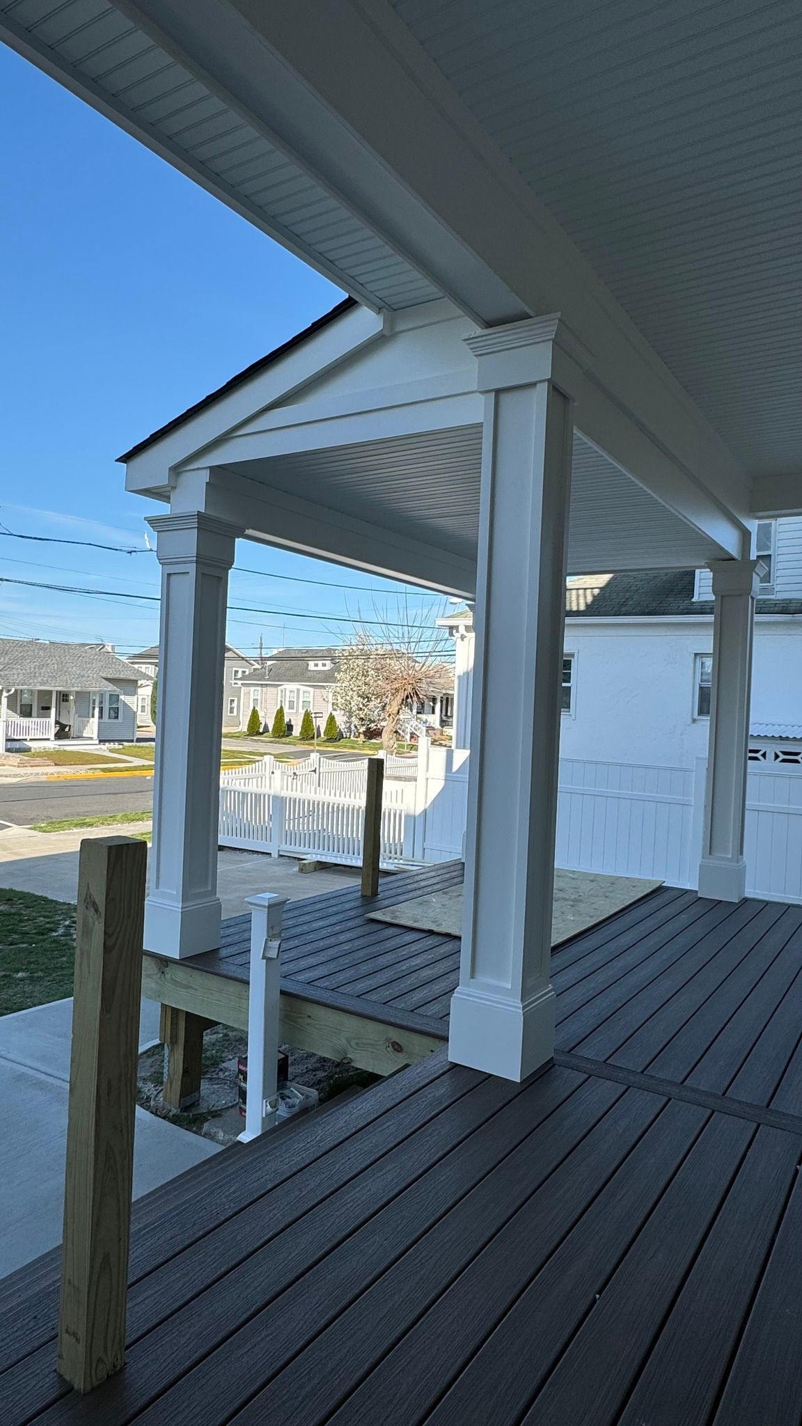 A porch with a wooden deck and a white house in the background