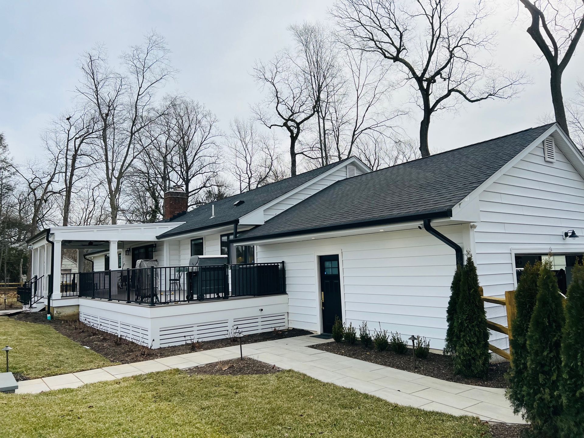 A white house with a black roof and a porch surrounded by trees
