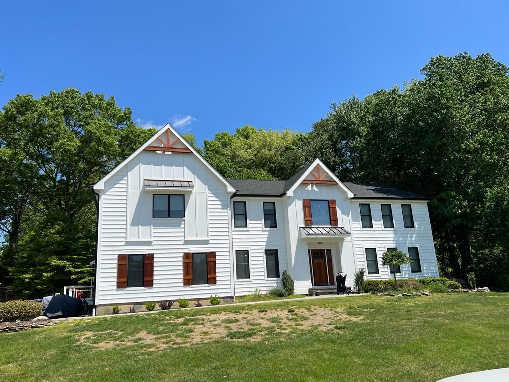 A large white house with black shutters is sitting on top of a lush green hill