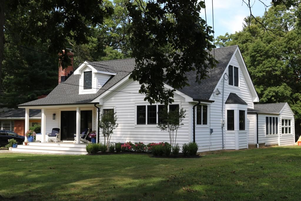 A white house with a black roof sits in the middle of a lush green field