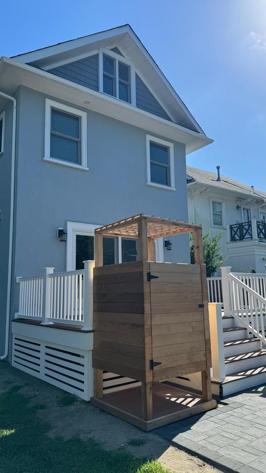 The back of a house with a wooden shower on the deck.